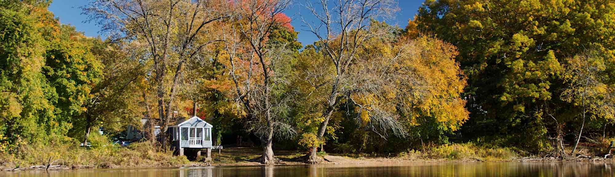 Shack near Bridge Street next to the Charles river with fall foliage.