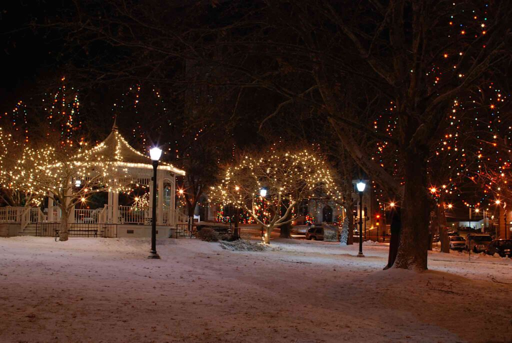 Gazebo in the snow with lights. Trash barrel is hidden and path is snow covered.