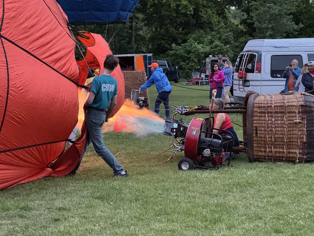 Crew member holds balloon open while pilot blasts burners